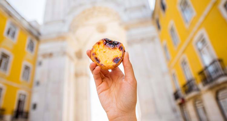 Mano sosteniendo un pastel de nata con un arco en el fondo.