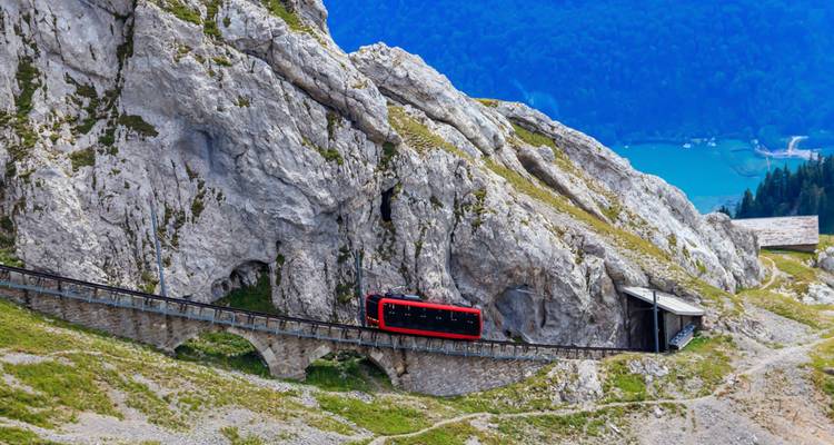 Red train traveling through mountainous terrain.