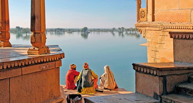Trois personnes assises au bord d'un lac serein entouré d'architecture historique.