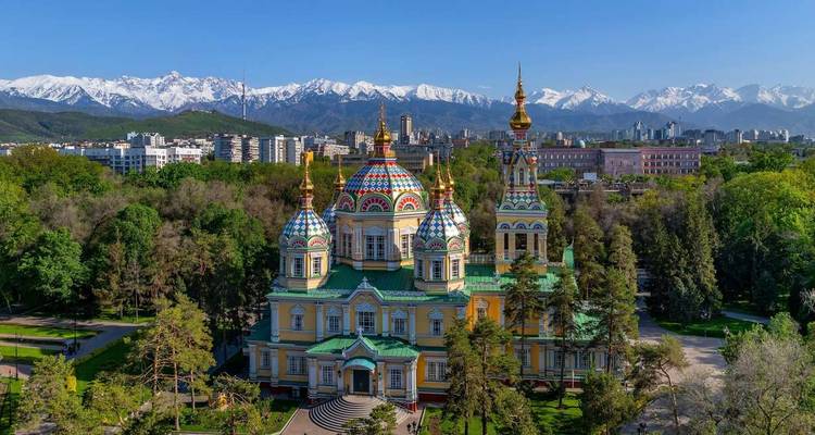 Kleurrijke kathedraal met besneeuwde bergen en stadsskyline op de achtergrond.