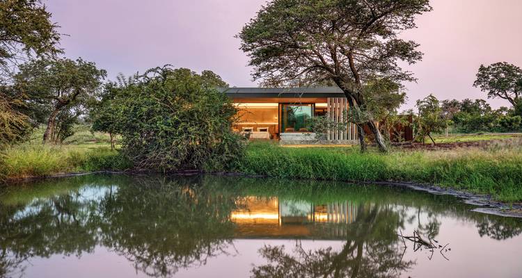 Maison moderne au bord d'un étang réfléchissant dans un cadre naturel.