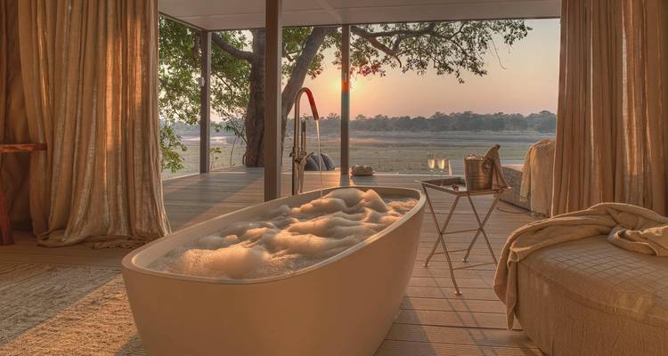 Baignoire luxueuse avec vue sur l'extérieur au coucher du soleil.