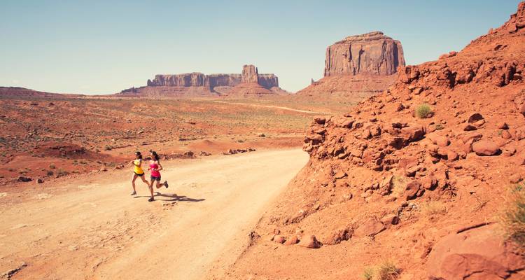 Two people running on a dirt road in a desert landscape.