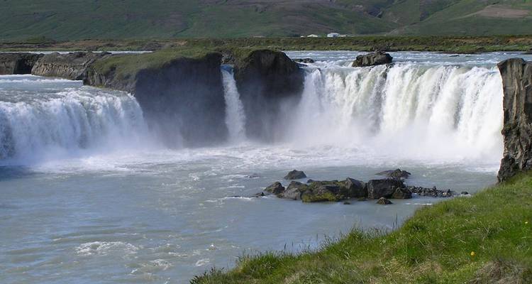 De brede waterval van Godafoss stort zich in sheets water over basaltrotsen in een melkachtige rivier.