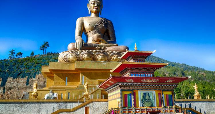 Gigantesca estatua dorada del Buda Dordenma que se eleva sobre un complejo de templos de varios niveles bajo un cielo azul profundo.