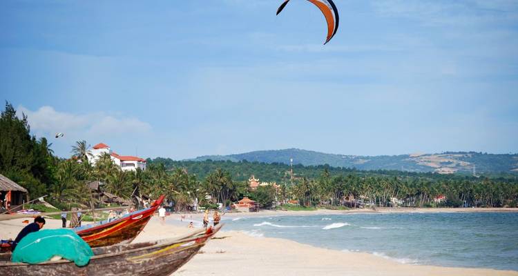Strand mit Booten und einem Kitesurfer.