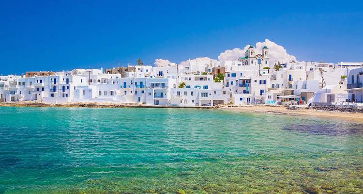 Row of cubic white Cycladic houses facing clear aquamarine sea beneath a brilliant sky