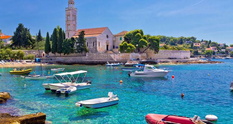 Baie turquoise cristalline avec des bateaux mouillés et une église en pierre sur l'île de Hvar.