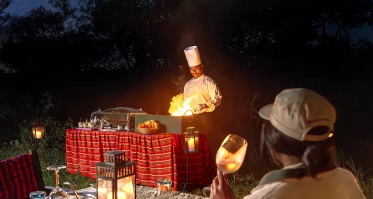 Ein Koch, der nachts im Freien kocht, mit einer Person, die am Tisch sitzt.