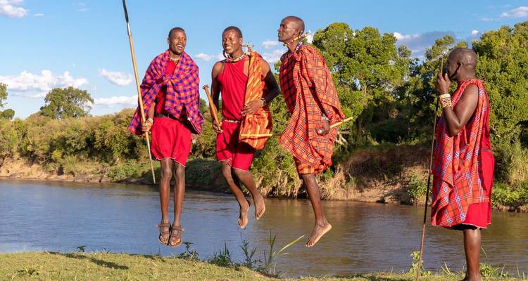 Menschen in traditioneller Kleidung springen an einem Fluss.