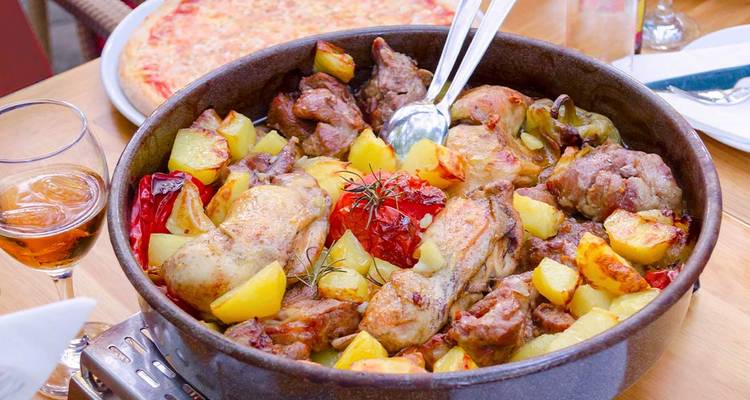 Traditional Balkan roast of meat, potatoes and peppers served in a metal pan on wooden table.