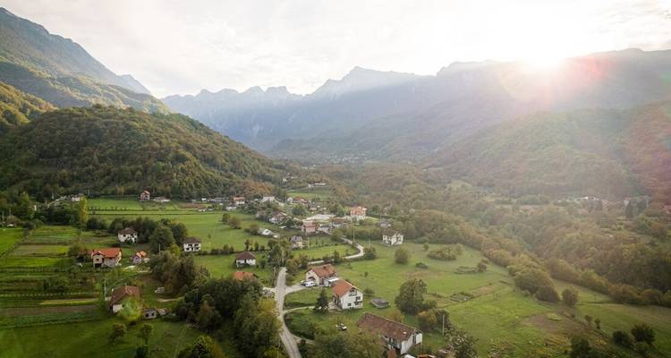 Aerial view of a verdant valley dotted with farms beneath a mountain range at sunrise