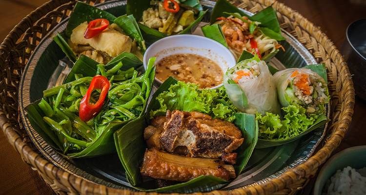 Colorful Vietnamese meal of vegetables, meats and spring rolls presented on banana leaves.
