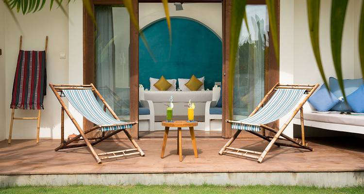 Two striped deckchairs and cocktails on a private bungalow terrace facing a garden.