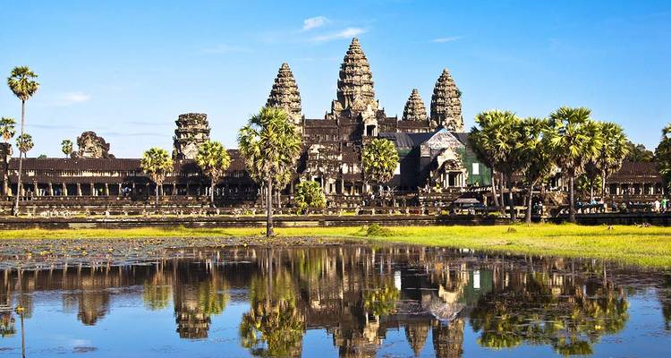 Angkor Wat temple complex reflected in a lotus pond under a bright blue sky.