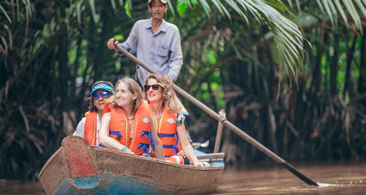 Tourists wearing life-jackets enjoy a small wooden boat ride through lush palms.