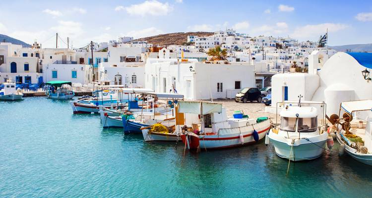 Kleurrijke vissersboten drijven naast helderwitte huizen in een kalme blauwe haven in Paros.