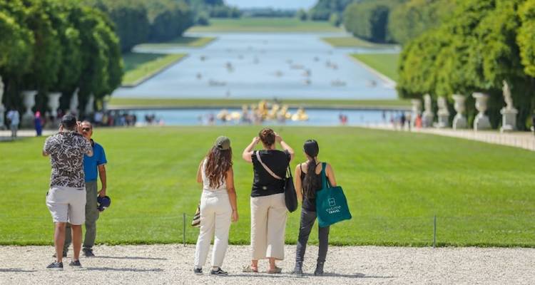 Besucher bewundern den Großen Kanal und die gepflegten Rasenflächen von Versailles von einer Kiestetrasse aus.