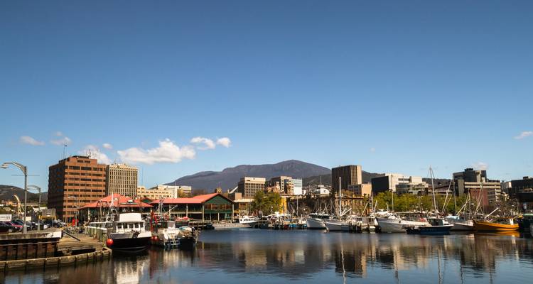 Vue du port avec bateaux et paysage urbain, montagnes en arrière-plan.