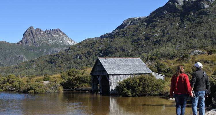 Couple se promenant près d'un hangar à bateaux avec des montagnes en arrière-plan.