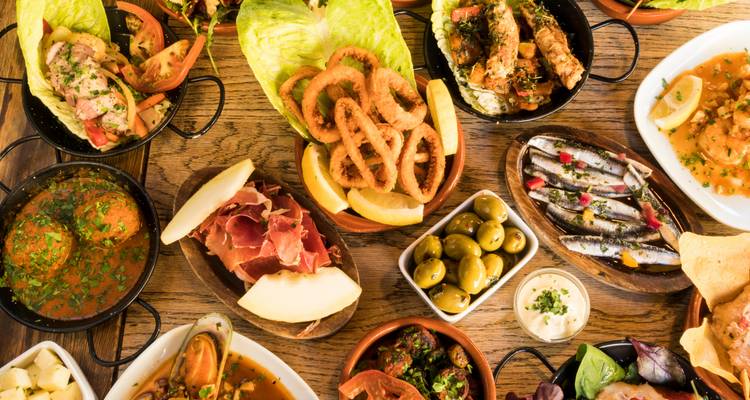 Tapas españolas variadas - aceitunas, jamón, calamares y mariscos - dispuestos en una mesa de madera rústica.
