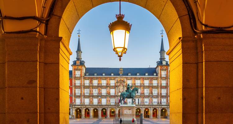 Plaza Mayor en Madrid enmarcada por un arco con la estatua ecuestre central iluminada por la cálida luz del atardecer.