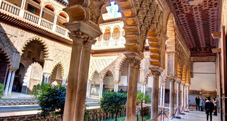Los arcos y columnas tallados con detalle bordean el pasillo del patio iluminado por el sol del Real Alcázar de Sevilla.