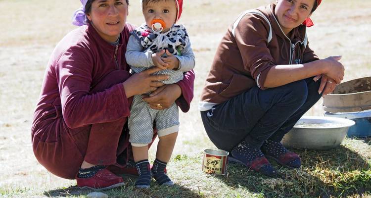 Two women and a baby sitting in a field.