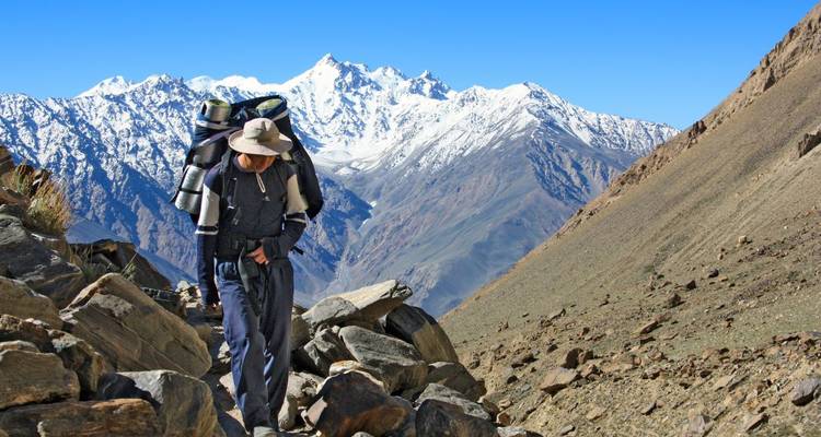 Hiker walking on a mountain trail with snowy peaks in the background.