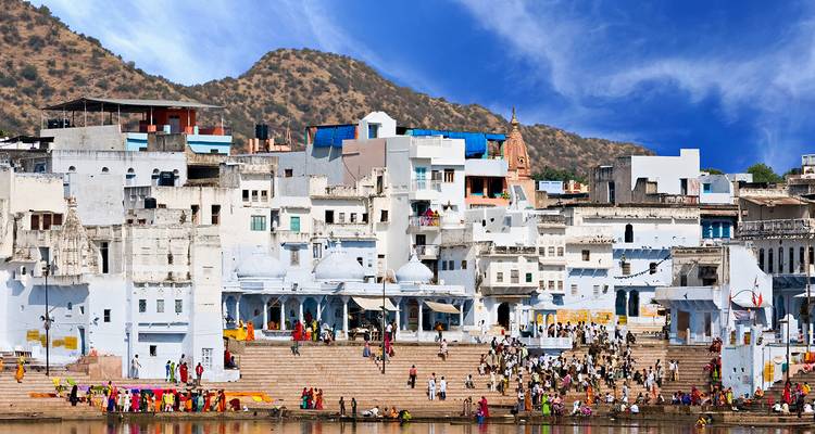 Pilgrims gather along the ghats of Pushkar Lake backed by whitewashed buildings and arid hills.