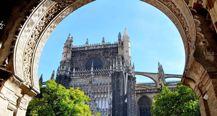 Die gotische Kathedrale von Sevilla, umrahmt von einem kunstvollen maurischen Bogen und grünen Orangenbäumen.