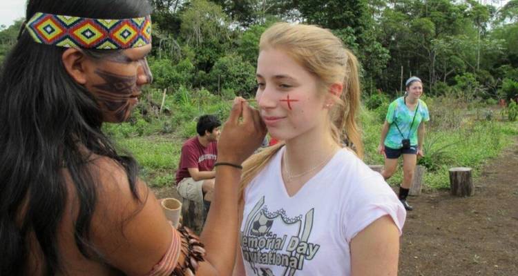 Inheemse gids schildert een rood symbool op de wang van een bezoeker tijdens culturele interactie in de jungle