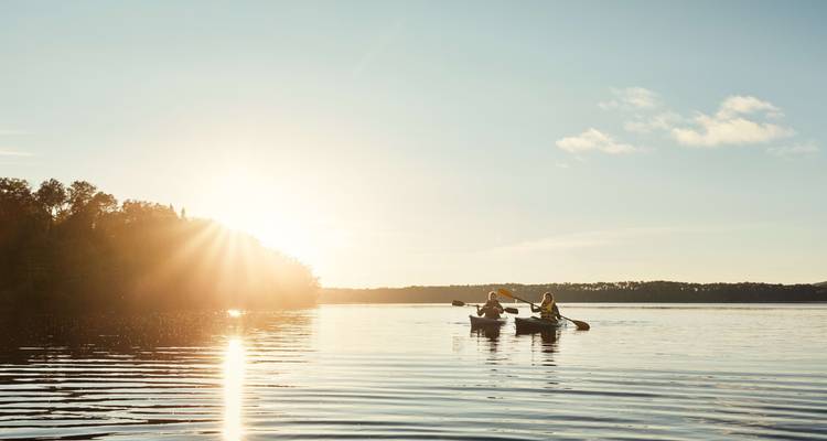 Zwei Kajakfahrer paddeln bei Sonnenuntergang auf einem See.