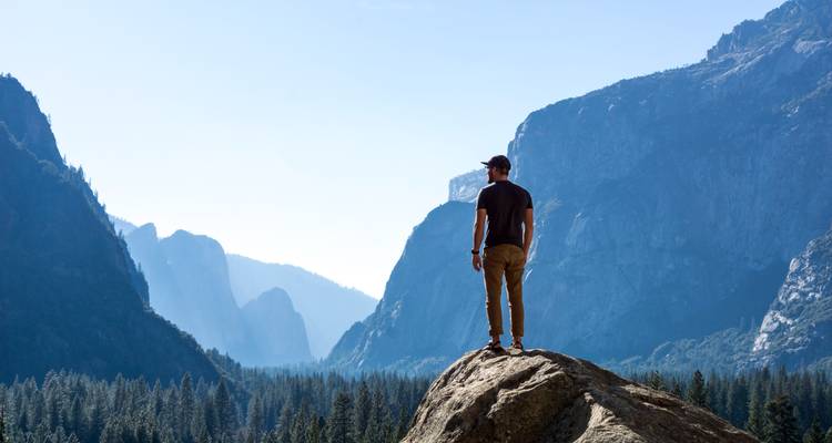 Man die op een rots staat en uitkijkt over een vallei in Yosemite.