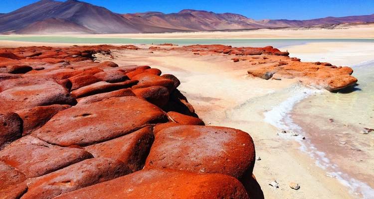Des rochers d'un roux éclatant mènent à un lagon turquoise situé face aux hautes terres andines arides.