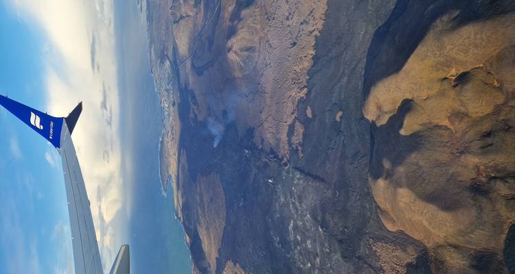 Aerial view from an Icelandair plane wing over rugged volcanic plains and distant coastline under blue sky