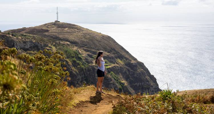 Hiker overlooking a scenic coastline with a visible lighthouse.