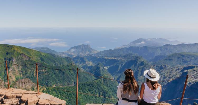 Two people viewing an expansive mountain landscape from a viewpoint.