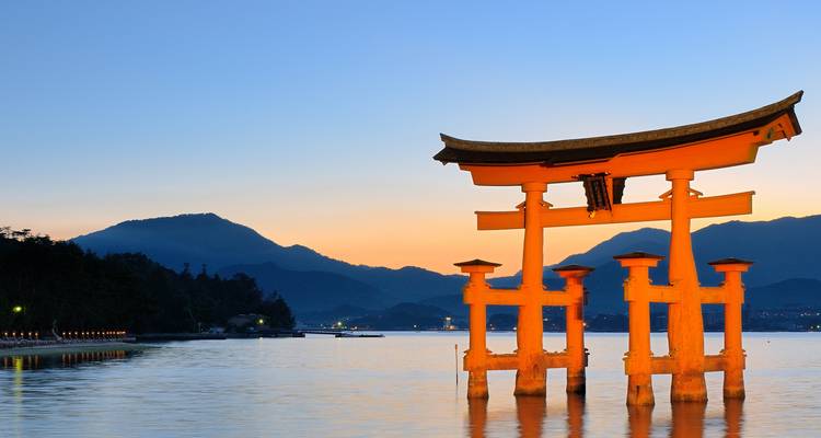 Ikonisches Torii-Tor, das bei Sonnenuntergang im Wasser steht.