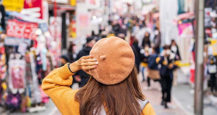 Back view of young woman in beret looking over a bustling, colorful street market in Tokyo.