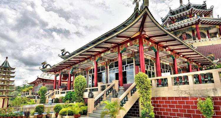 Ornate red-and-green Taoist Temple with dragon statues and terraces under cloudy sky.
