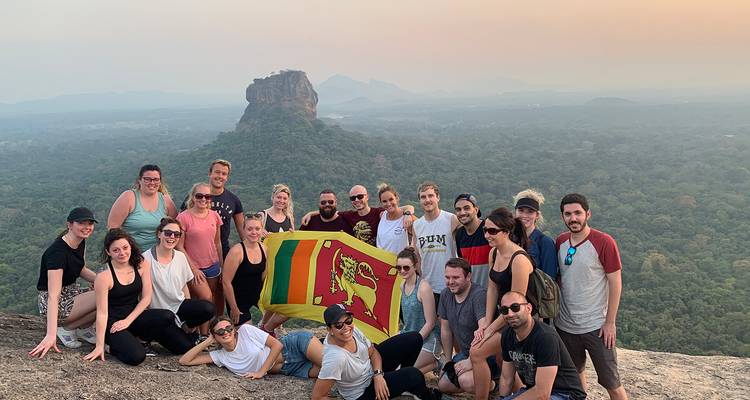 Grote groep mensen op een heuvel met een vlag, Sigiriya rots zichtbaar.