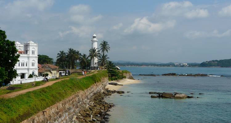 Uitzicht op een vuurtoren en een oud fort aan zee met bewolkte luchten.