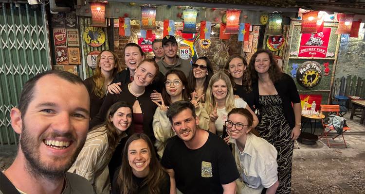 Group selfie inside a colorful Hanoi alley bar decorated with lanterns and retro signs.