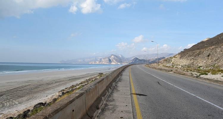 Carretera costera que corre junto a una playa prístina y vacía con montañas distantes.