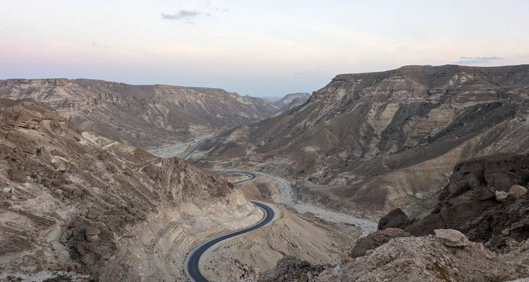 Serpenteante carretera de montaña que serpentea a través de escarpados valles rocosos al anochecer.