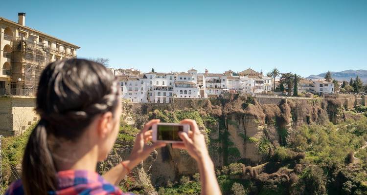 Persona tomando una foto de un pueblo en lo alto de un acantilado.