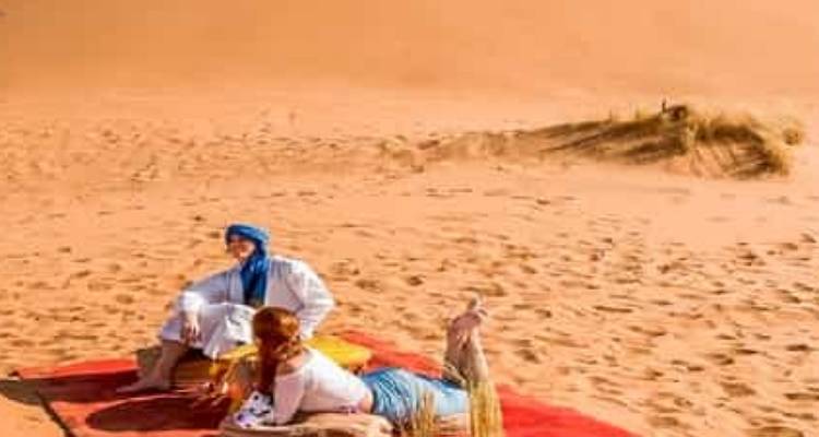 Two people relaxing on a red carpet in a sandy desert