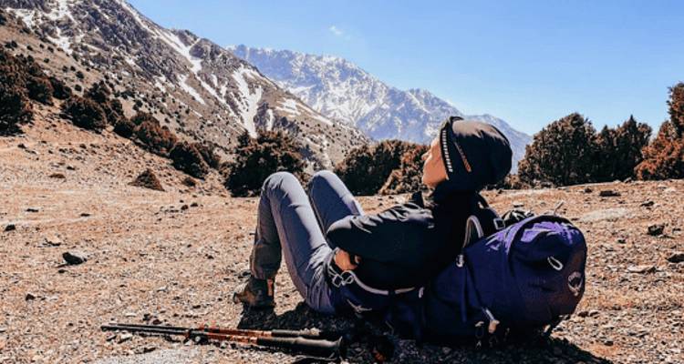Person resting on a hiking trail with scenic mountain views.