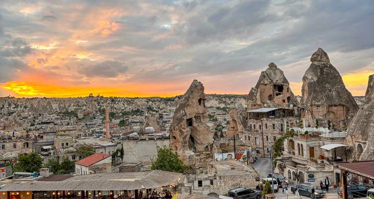 Historic stone dwellings and fairy chimneys of Göreme town lit by a dramatic sunset sky.